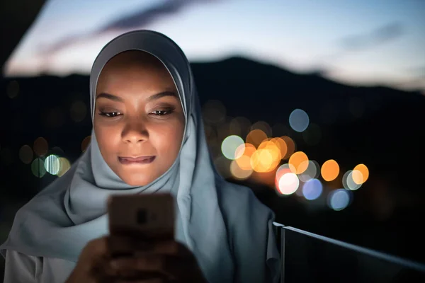 Ung Muselman kvinna på gata på natten användande telefon Royaltyfria Stockfoton