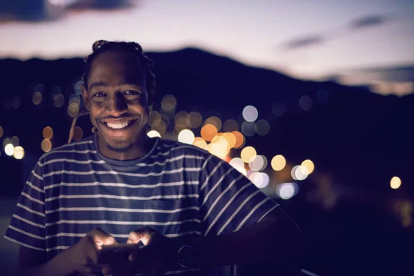 Jovem afro homem na rua à noite usando telefone — Fotografia de Stock