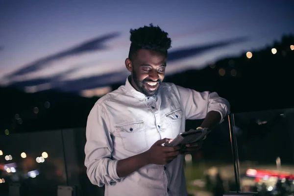 Mladý Afro muž na ulici v noci pomocí telefonu — Stock fotografie