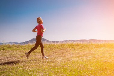 Genç bir kadın yaz dağında güneşli bir günde koşuyor.
