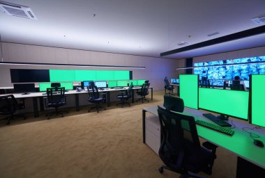 Boş yeşil ekranlı büyük modern güvenlik kontrol odasının içi, birden fazla ekranı olan çalışma istasyonu, güvenlik veri merkezindeki izleme odası boş ofis, masa ve ana CCTV veri merkezindeki sandalyeler.