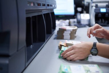 Banka çalışanları banka kasasında kağıt banknotları sıralarken ve sayarken para sayma makinesi kullanıyorlar. Bankada büyük miktarda para var.