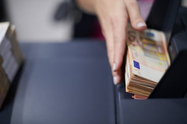 Banka çalışanları banka kasasında kağıt banknotları sıralarken ve sayarken para sayma makinesi kullanıyorlar. Bankada büyük miktarda para var.