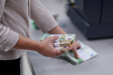Banka çalışanları banka kasasında kağıt banknotları sıralarken ve sayarken para sayma makinesi kullanıyorlar. Bankada büyük miktarda para var.