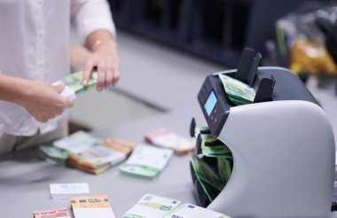 Banka çalışanları banka kasasında kağıt banknotları sıralarken ve sayarken para sayma makinesi kullanıyorlar. Bankada büyük miktarda para var.