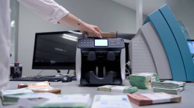 Banka çalışanları banka kasasında kağıt banknotları sıralarken ve sayarken para sayma makinesi kullanıyorlar. Bankada büyük miktarda para var.