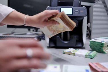 Banka çalışanları banka kasasında kağıt banknotları sıralarken ve sayarken para sayma makinesi kullanıyorlar. Bankada büyük miktarda para var.