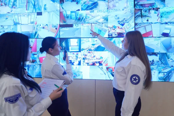 在数据系统控制室工作的一组女性安全操作员技术操作员在有多个显示器的工作站工作 保安人员在监视室操作多个监视器 监测Cctv并讨论 — 图库照片