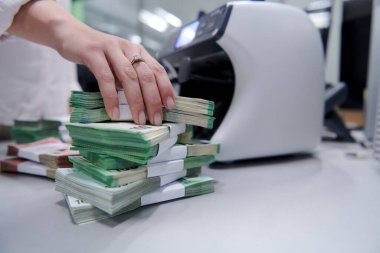 Banka çalışanları banka kasasında kağıt banknotları sıralarken ve sayarken para sayma makinesi kullanıyorlar. Bankada büyük miktarda para var.