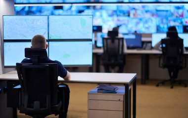 Veri kontrol odası ofislerinde çalışan erkek güvenlik operatörü. Çalışma istasyonunda birden fazla ekranla çalışan teknik operatör. Güvenlik merkezinden birden fazla monitörde çalışan güvenlik görevlisi.