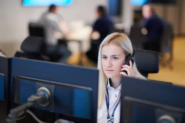 Female security guard operator talking on the phone while working at workstation with multiple displays Security guards working on multiple monitors