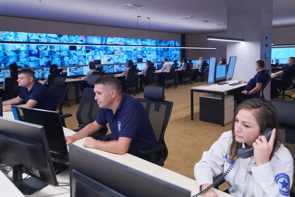 在闭路电视监控室工作的一组保安数据中心操作员看着多个监控员监控可疑活动的多屏风小组在系统控制室工作 — 图库照片