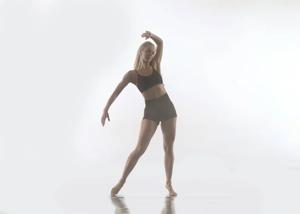 穿着黑色紧身衣的年轻漂亮女体育舞蹈家表演现代风格的芭蕾舞 在白人背景下表演杂技演员 — 图库照片