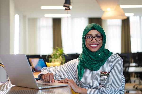 african muslim business woman wearing a green hijab while working on laptop computer in relaxation area at modern open plan startup office. Diversity, multiracial concept