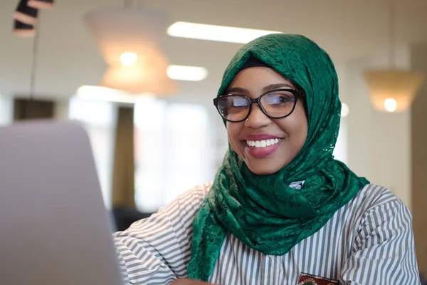 アフリカのイスラム教徒のビジネス女性は緑のヒジャーブを身に着けている現代のオープンプランのスタートアップオフィスのリラクゼーションエリアでラップトップコンピュータに取り組んでいる間 多様性 多人種的概念 — ストック写真