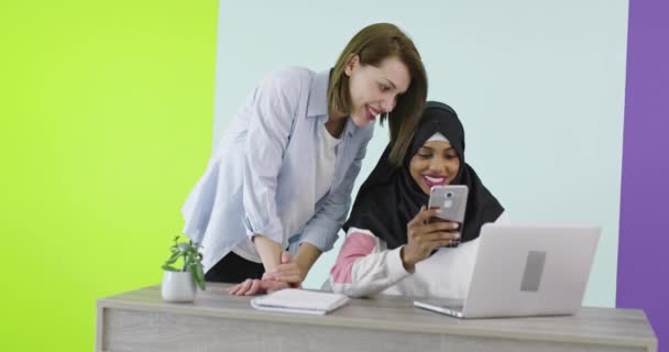 Встреча этнических женщин в офисе. Улыбающаяся девушка в хиджабе работает над ноутбуком, блондинка смотрит на экран. — стоковое видео