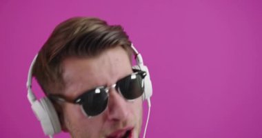 Genç yakışıklı adam stüdyonun renkli arka planında kulaklık takmaktan mutlu.