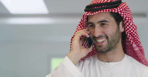 家庭でスマートフォンを使いながら伝統的な衣服を身に着けている若い現代のイスラム教徒のアラビア人ビジネスマン — ストック動画