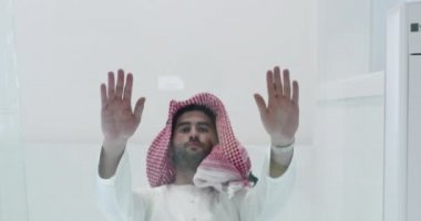Geleneksel giysiler içinde Müslüman bir adam iftar yemeğinden önce cam zeminde dua ediyor.