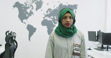 Yeşil başörtülü Afrikalı Müslüman kadın müşteri temsilcisi telefon kulaklıklı iş kadını modern çağrı merkezindeki müşterilere internet üzerinden yardım ve destek veriyor.