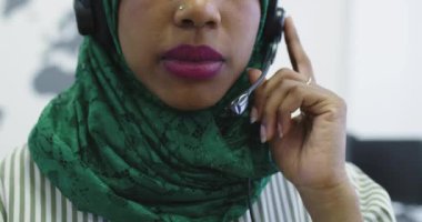 Yeşil başörtülü Afrikalı Müslüman kadın müşteri temsilcisi telefon kulaklıklı iş kadını modern çağrı merkezindeki müşterilere internet üzerinden yardım ve destek veriyor.