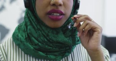 Yeşil başörtülü Afrikalı Müslüman kadın müşteri temsilcisi telefon kulaklıklı iş kadını modern çağrı merkezindeki müşterilere internet üzerinden yardım ve destek veriyor.