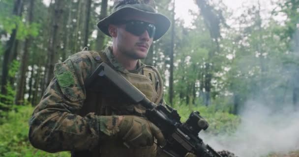 Сучасний солдат з рушницею в густому лісі з димом в задньому плані — стокове відео