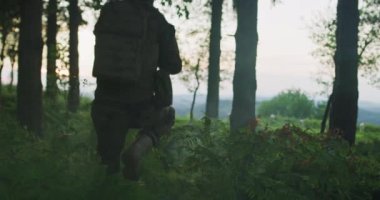 Bir adamın silueti ve ormanda çimlerin üzerinde yürüyen bir sırt çantası. İnsanoğlu ormanda seyahat ediyor..