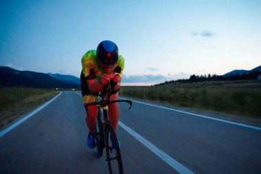 Triatlon atleti gece sporunda profesyonel yarış bisikleti sürüyor.