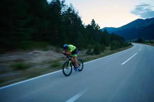 三项全能运动员在弯弯曲曲的乡间道路上骑职业自行车进行夜间训练 — 图库照片