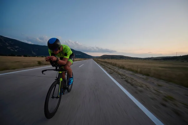 三项全能运动员在弯弯曲曲的乡间道路上骑职业自行车进行夜间训练 — 图库照片