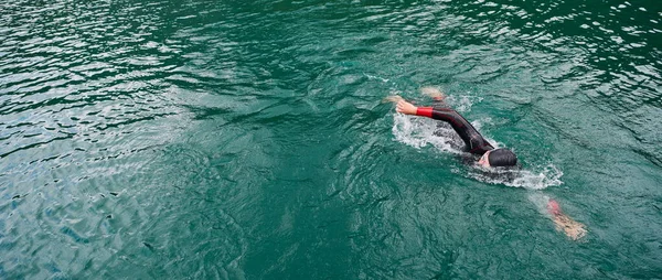 triathlon athlete swimming on lake wearing wetsuit