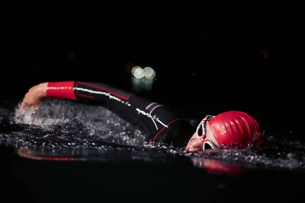 Atleta de triatlón nadando en la noche oscura usando traje de neopreno — Foto de Stock