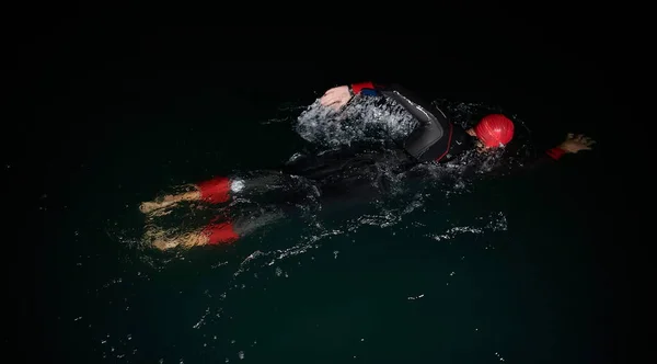 Triatlon atleti karanlık gecede yüzüyor. Dalış kıyafeti giyiyor. — Stok fotoğraf