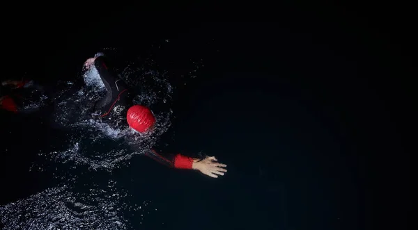 Atleta triatlo nadando na noite escura vestindo roupa de mergulho — Fotografia de Stock