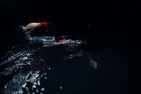 Atleta di triathlon che nuota nella notte scura indossando muta — Foto Stock