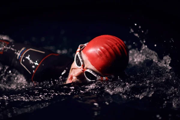 Atleta de triatlón nadando en la noche oscura usando traje de neopreno — Foto de Stock