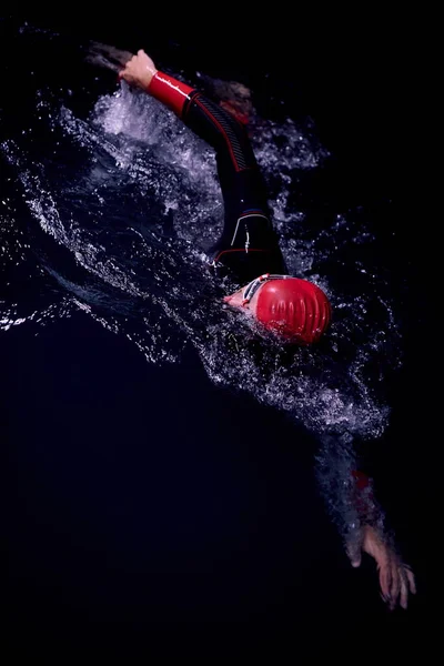 triathlon athlete swimming in dark night wearing wetsuit