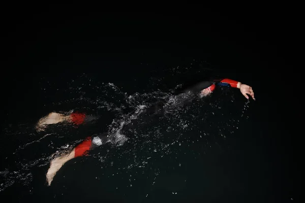 Athlète de triathlon nageant dans la nuit noire portant une combinaison — Photo