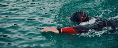 Triatlon sporcusu gün doğumunda gölde yüzüyor. Dalgıç kıyafeti giyiyor.