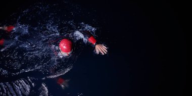 Triatlon atleti karanlık gecede yüzüyor. Dalış kıyafeti giyiyor.