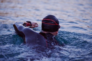 Triatlon sporcusu gün doğumunda gölde yüzüyor. Dalgıç kıyafeti giyiyor.