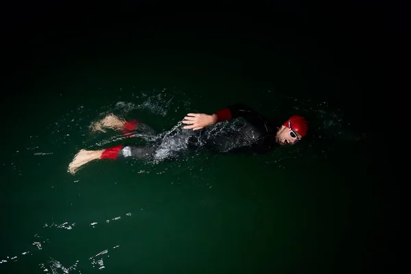 Atleta di triathlon che nuota nella notte scura indossando muta — Foto Stock
