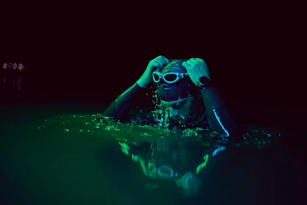 Autêntico triatleta nadador tendo uma pausa durante o treinamento duro na noite neon gel luz — Fotografia de Stock