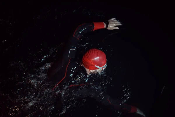 Athlète de triathlon nageant dans la nuit noire portant une combinaison — Photo