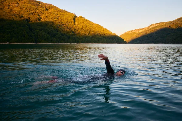 Спортсмен тріатлону, який плаває на озері на сході сонця в гідрокостюмі — стокове фото