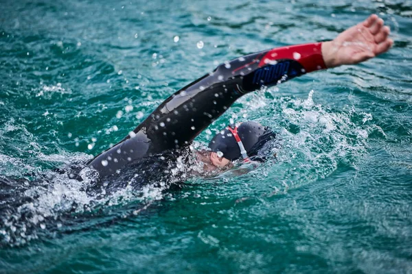 Triatlon atléta úszás tavon napkeltekor búvárruhában — Stock Fotó