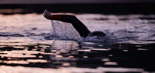 Atleta de triatlón nadando en el lago al amanecer usando traje de neopreno — Foto de Stock