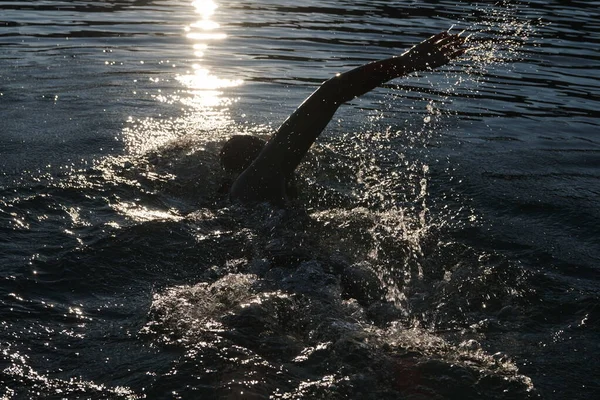 Atleta di triathlon che nuota sul lago all'alba indossando la muta — Foto Stock