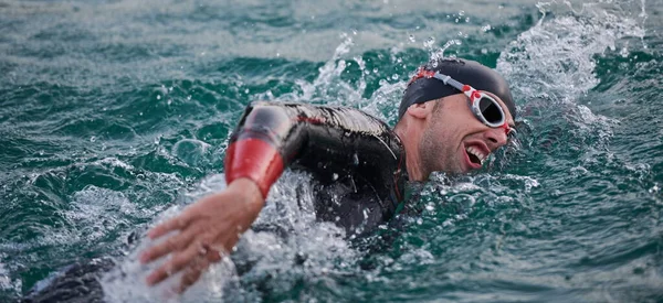 Triathlet schwimmt bei Sonnenaufgang im Neoprenanzug auf See — Stockfoto